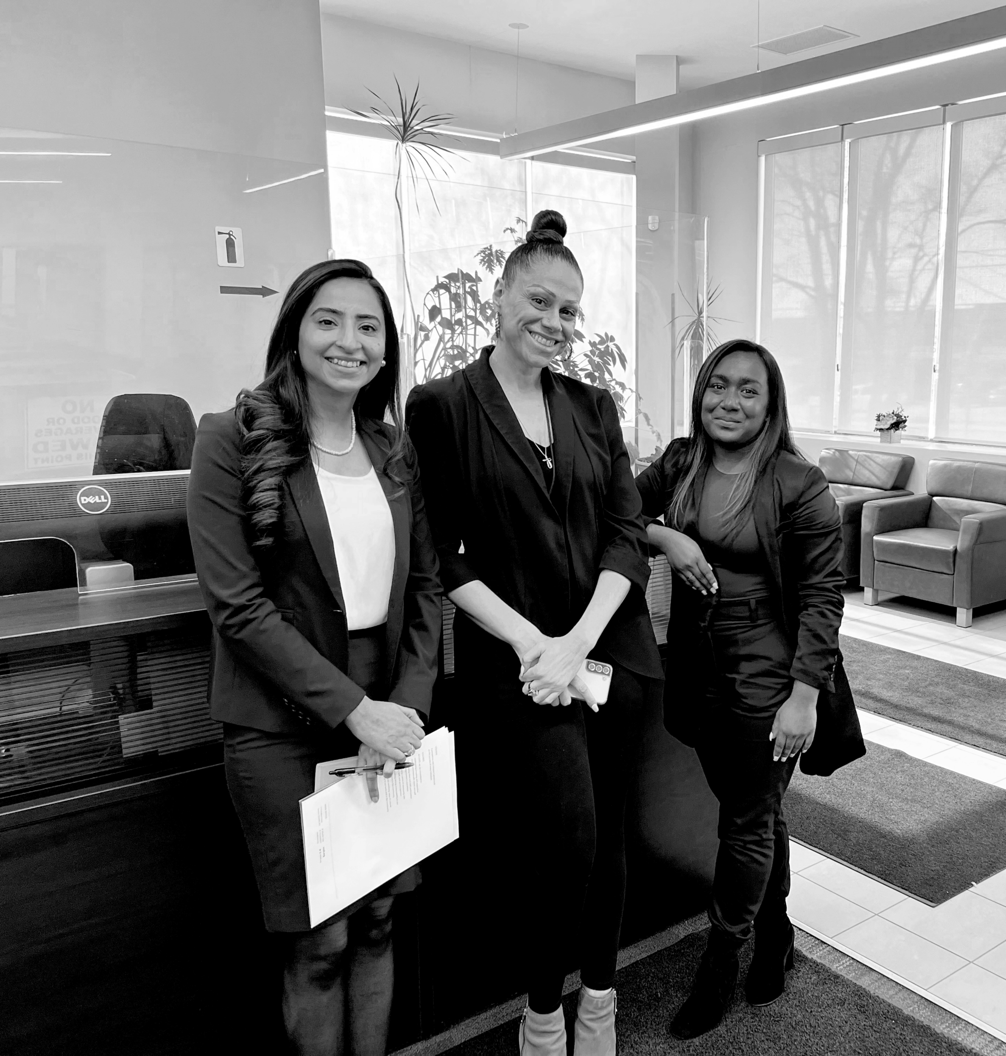 A group of three diverse women standing next to each other with warm smiles on their faces, in an office reception area