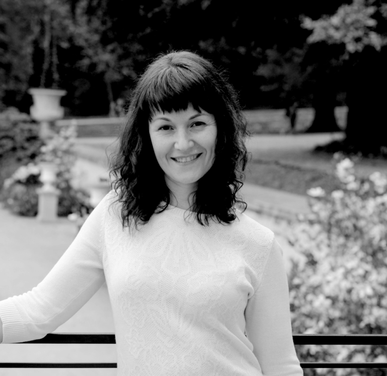 Olena, a successful client of COSTI’s Education Division is standing at a railing in a garden, smiling and posing